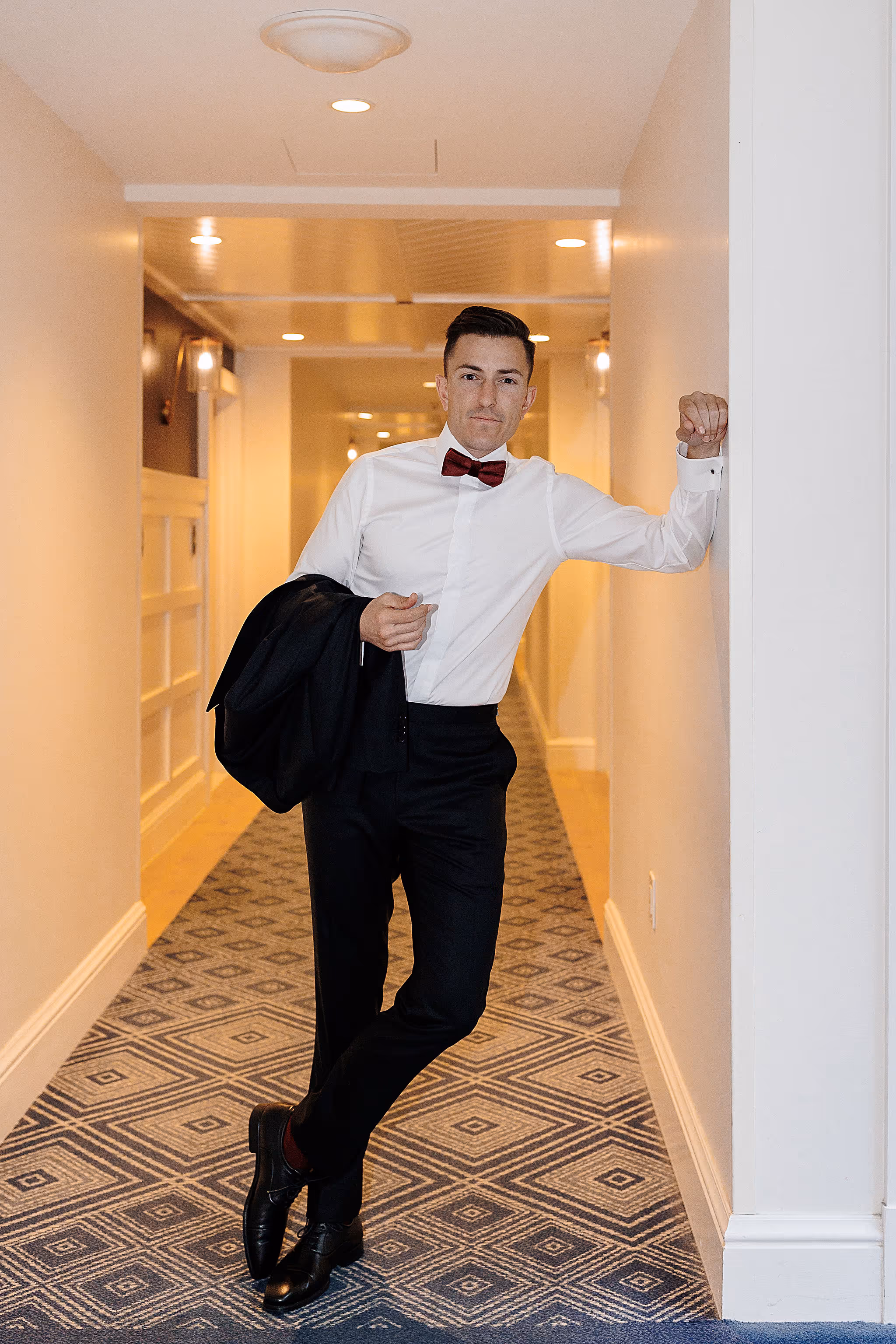 Groom confidently walking down hallway with jacket over shoulder at Lido House