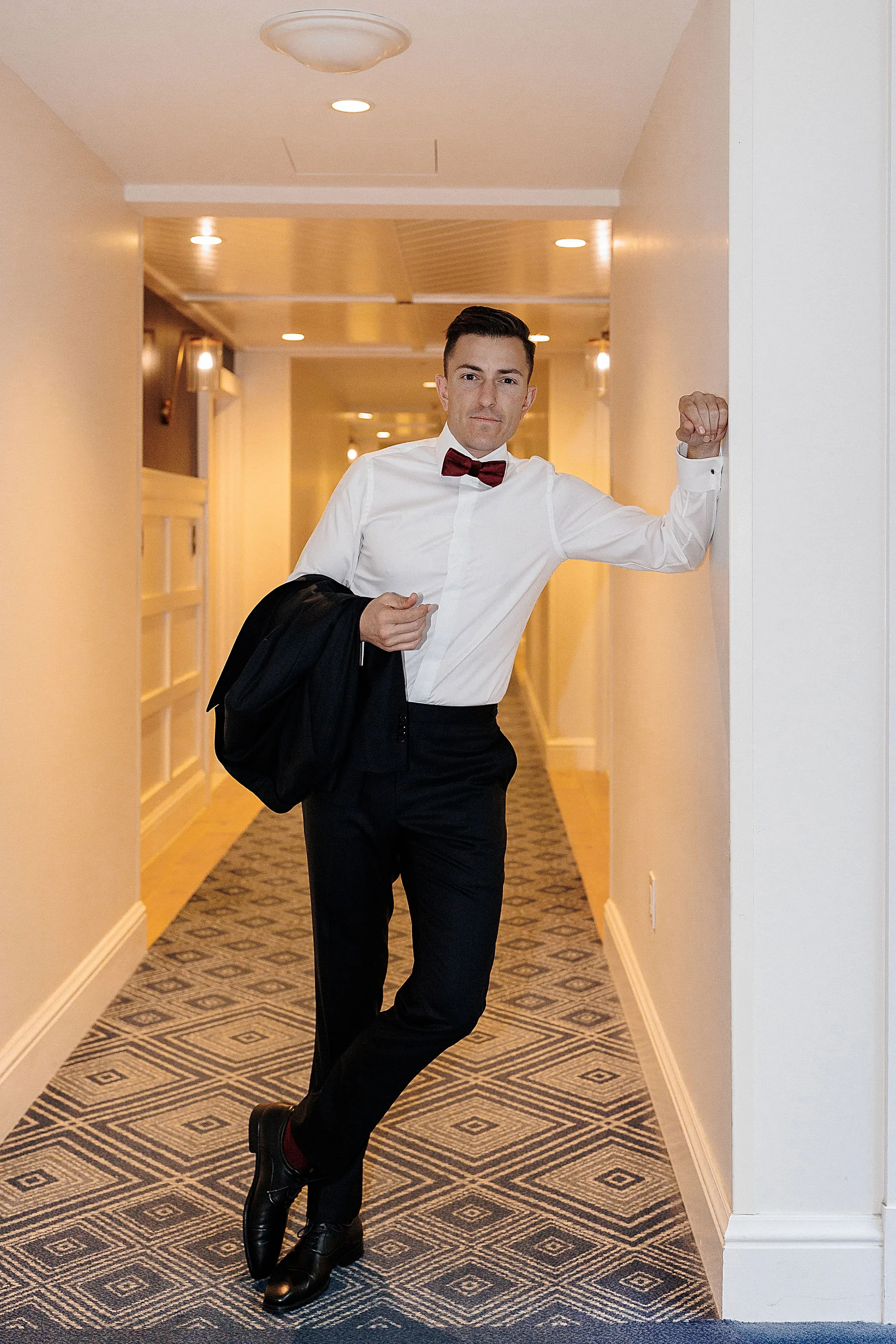 Groom confidently walking down hallway with jacket over shoulder at Lido House