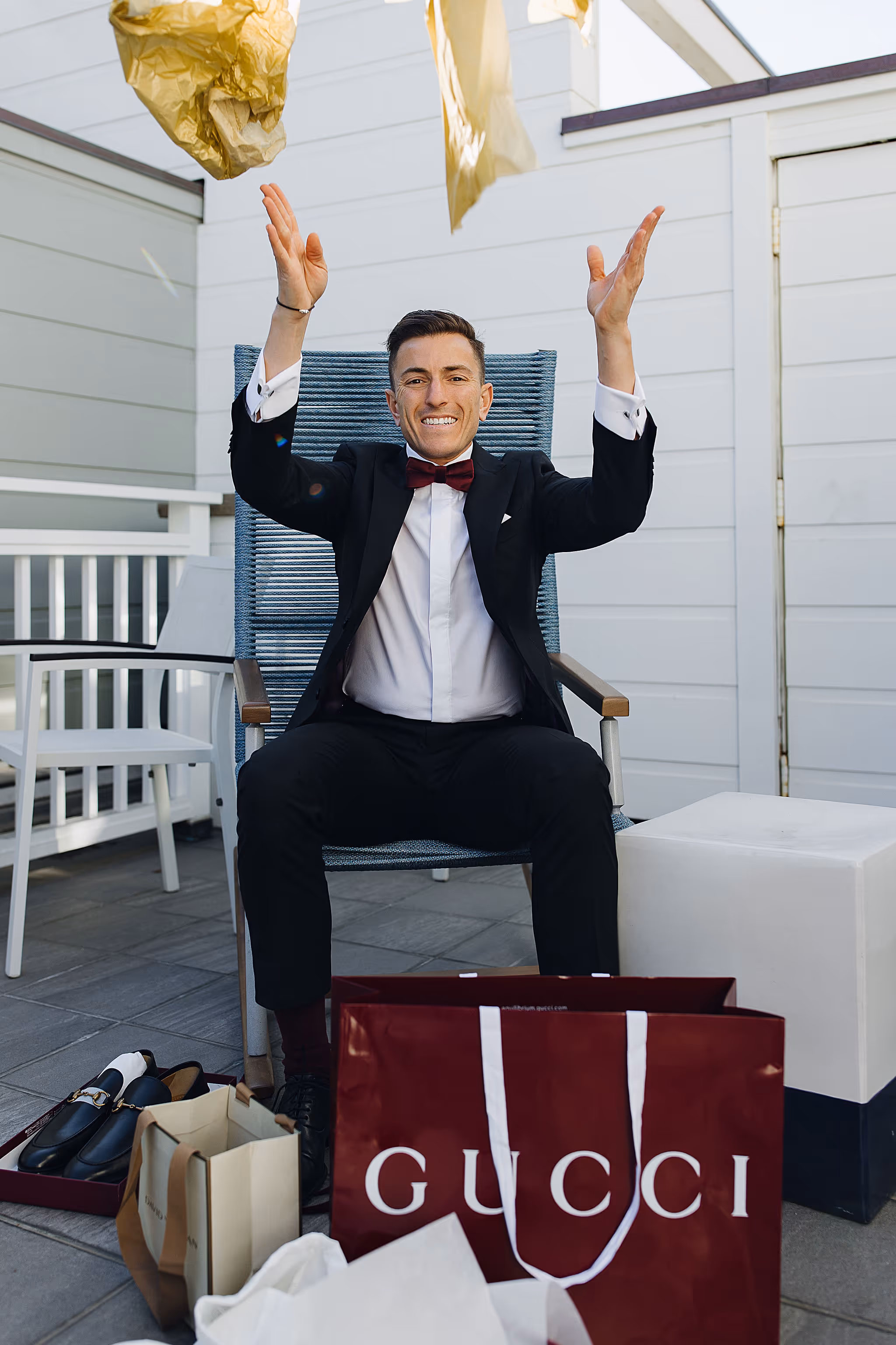 Groom playfully raising arms seated with shopping bags at Lido House