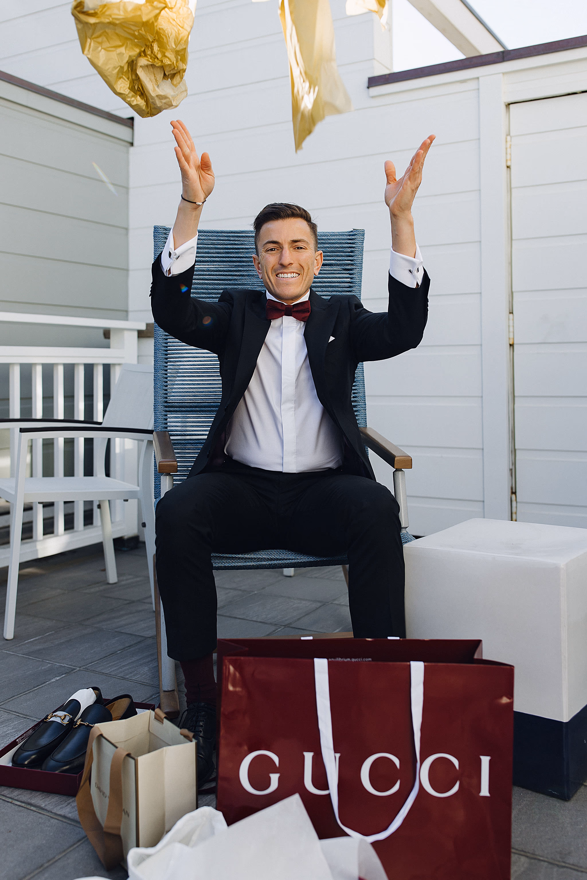 Groom playfully raising arms seated with shopping bags at Lido House