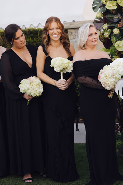 Bridesmaids in black dresses holding white bouquets at Lido House
