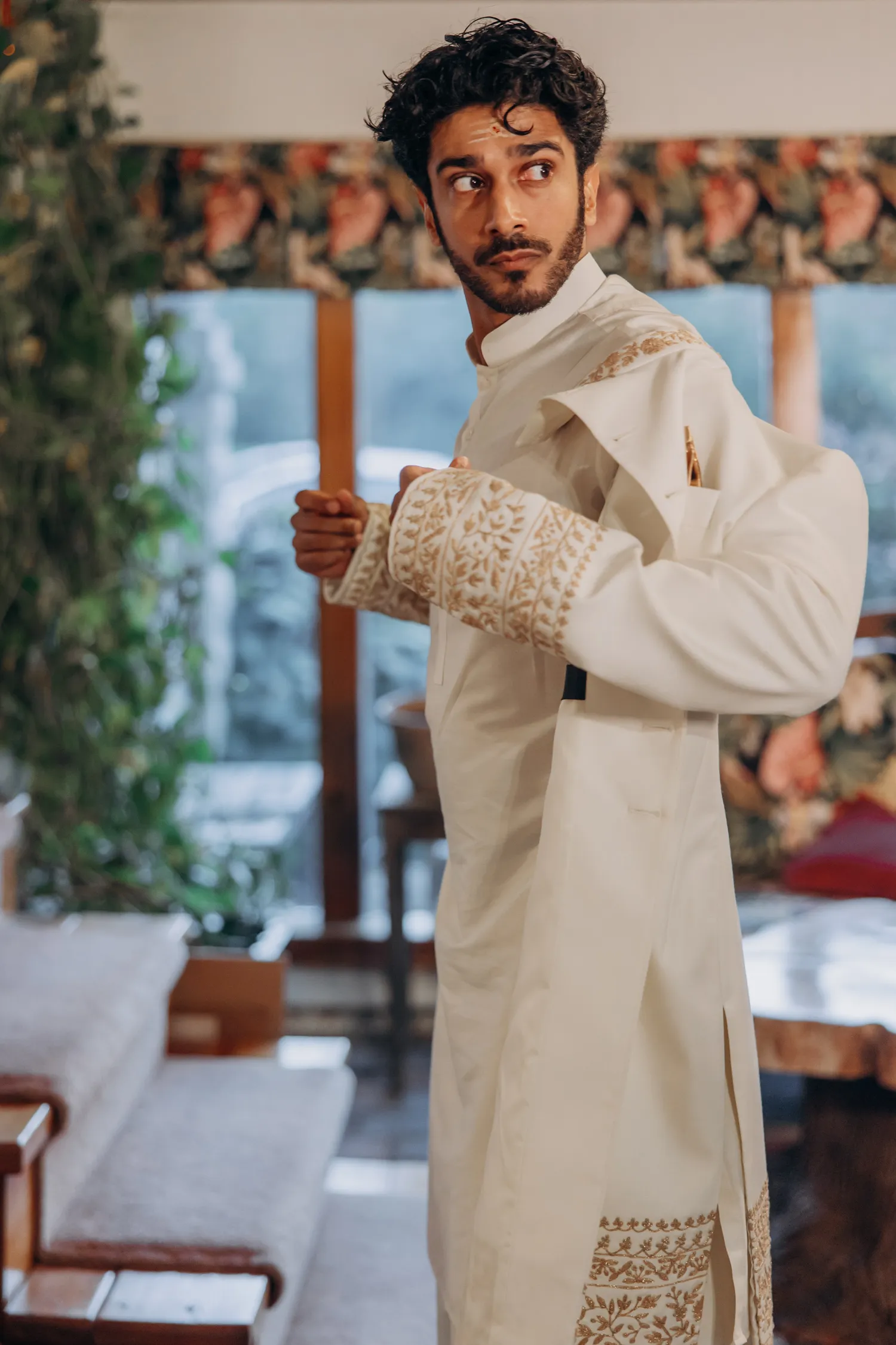 Groom in white sherwani looking out before Madison Greenhouse Tamil outdoor wedding